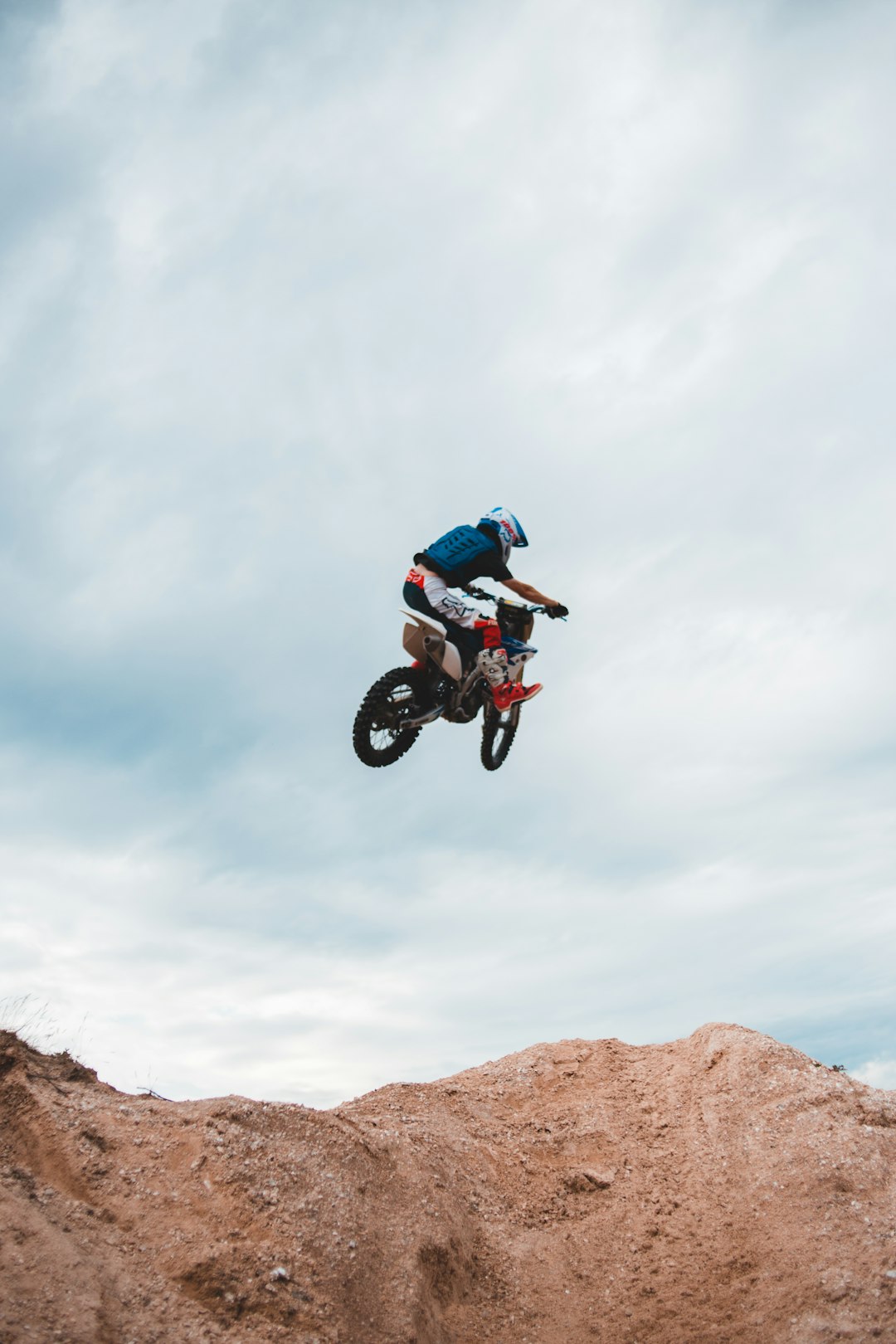 man in blue jacket riding motocross dirt bike on brown rocky mountain under white cloudy sky