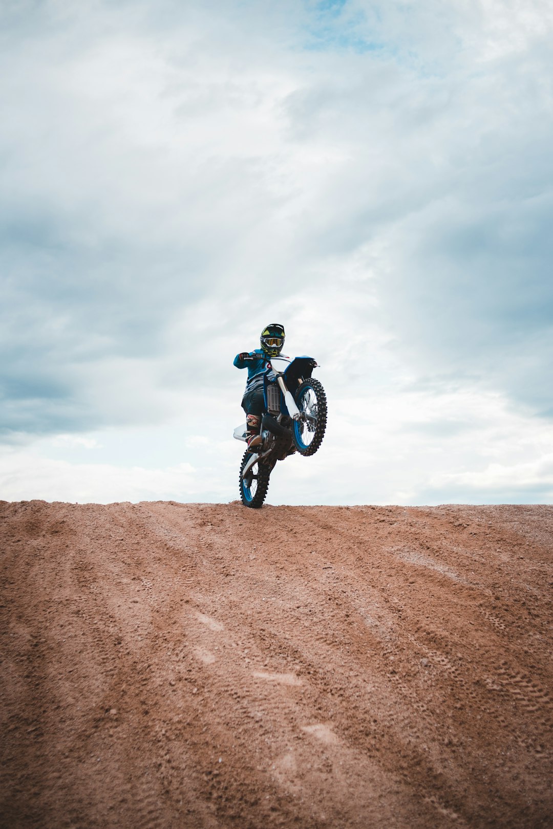 man in black jacket riding on black motorcycle on brown sand under white cloudy sky during