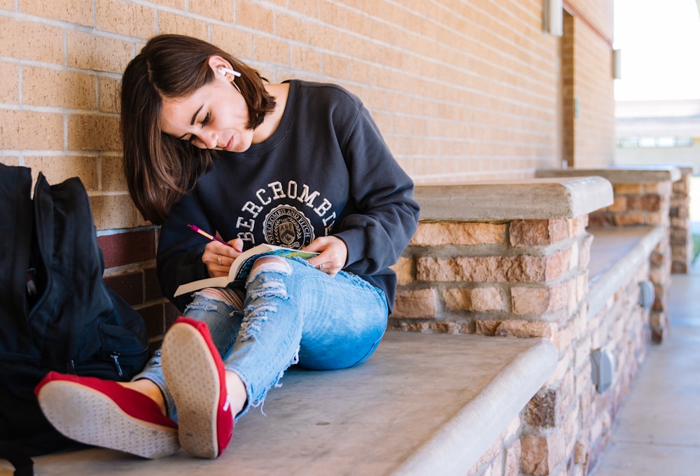 woman in black hoodie and blue denim jeans sitting on concrete stairs