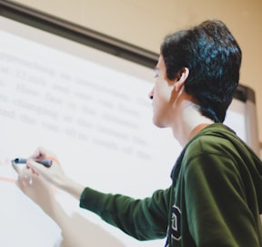 man in green and white long sleeve shirt writing on a white board