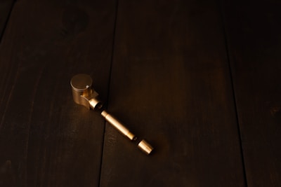 A metallic object, possibly a pipe or a mechanical part, is placed on a dark wooden surface. The object appears to be made of brass or a similar golden-colored metal.
