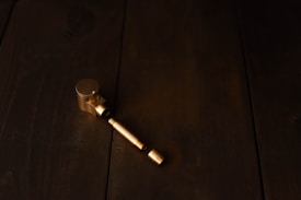 A metallic object, possibly a pipe or a mechanical part, is placed on a dark wooden surface. The object appears to be made of brass or a similar golden-colored metal.