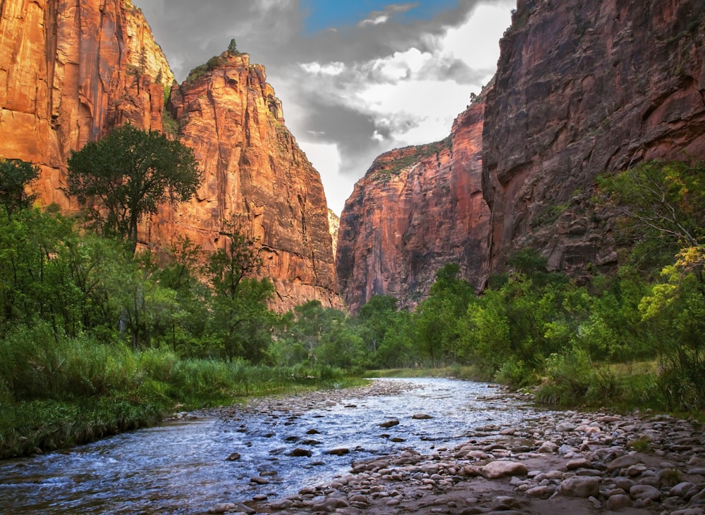 brown rocky mountain beside green trees under white clouds and blue sky during daytime