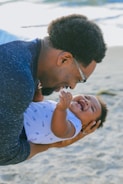 man in blue sweater kissing woman in white and blue polka dot shirt on beach during