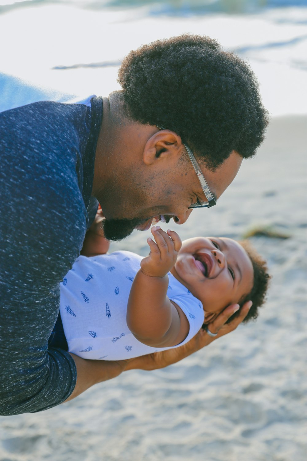 man in blue sweater kissing woman in white and blue polka dot shirt on beach during