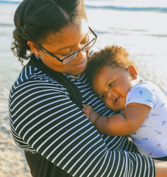 woman in black and white striped shirt carrying baby in white and blue onesie