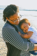 woman in black and white striped shirt carrying baby in white and blue onesie