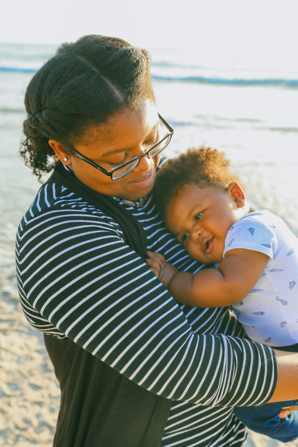 woman in black and white striped shirt carrying baby in white and blue onesie