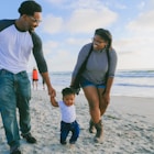 man in black and white striped long sleeve shirt holding baby in white shirt on beach