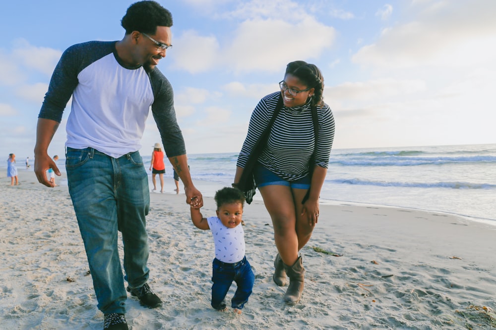 man in black and white striped long sleeve shirt holding baby in white shirt on beach