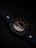 A watch with a dark leather strap and a metallic case, featuring a black dial with contrasting white and gold numerals and hands, is positioned at an angle. The background is subtly lit in dark tones, enhancing the sleek and elegant design of the watch.