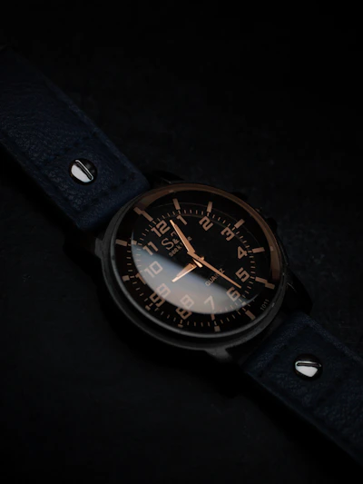 Elegant watch with a matte black dial and simple hour markers, paired with a smooth black leather strap on a wooden table.