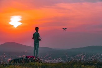 Operator controlling drone with remote in a sunny farm setting.