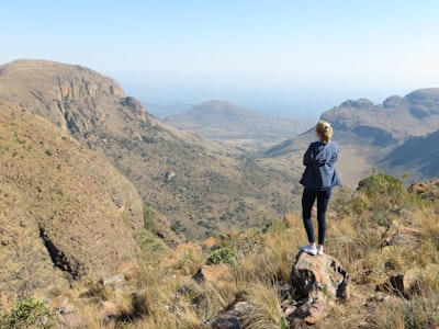 man in black t-shirt and blue denim shorts standing on brown rock mountain during daytime wilderness google meet background