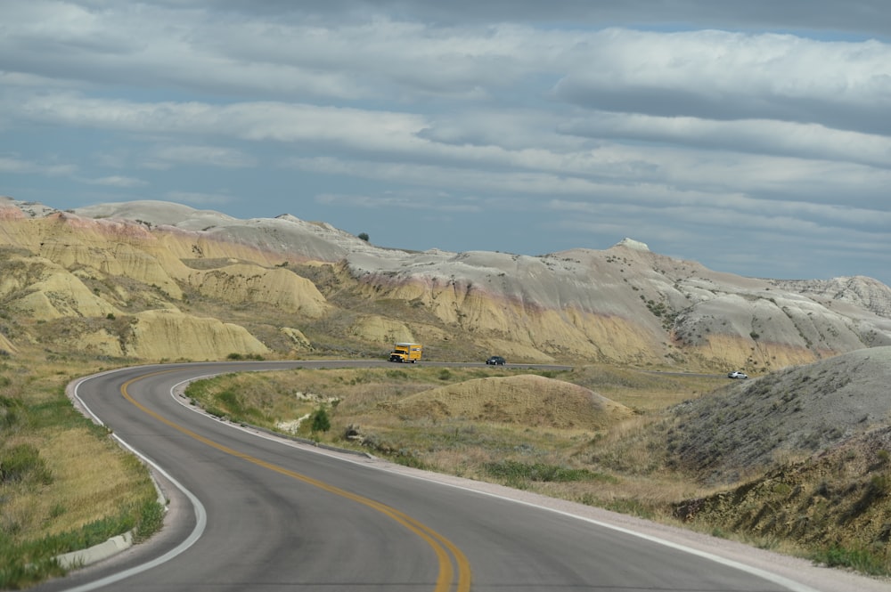 estrada de asfalto cinza perto da montanha marrom sob nuvens brancas durante o dia