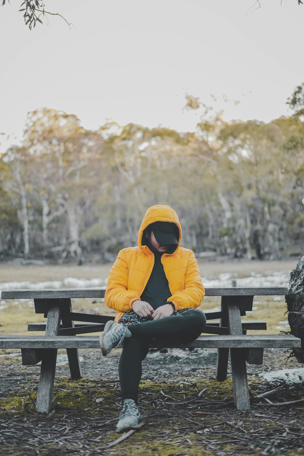 woman in yellow hoodie sitting on brown wooden bench during daytime