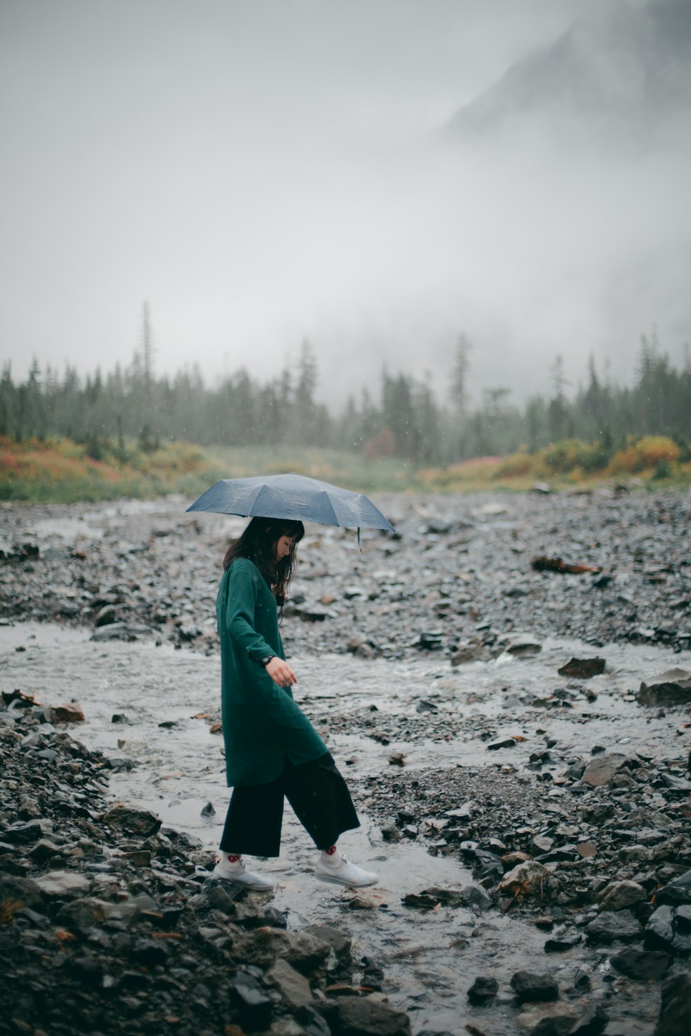 woman in green jacket holding umbrella walking on rocky ground during daytime