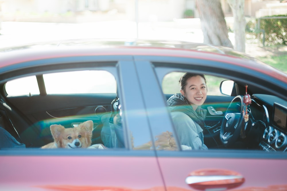 man in blue dress shirt driving red car with brown dog during daytime