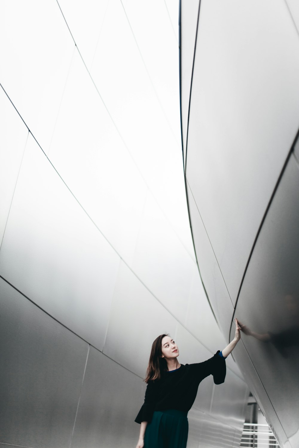 Donna in camicia nera a maniche lunghe in piedi accanto al muro bianco