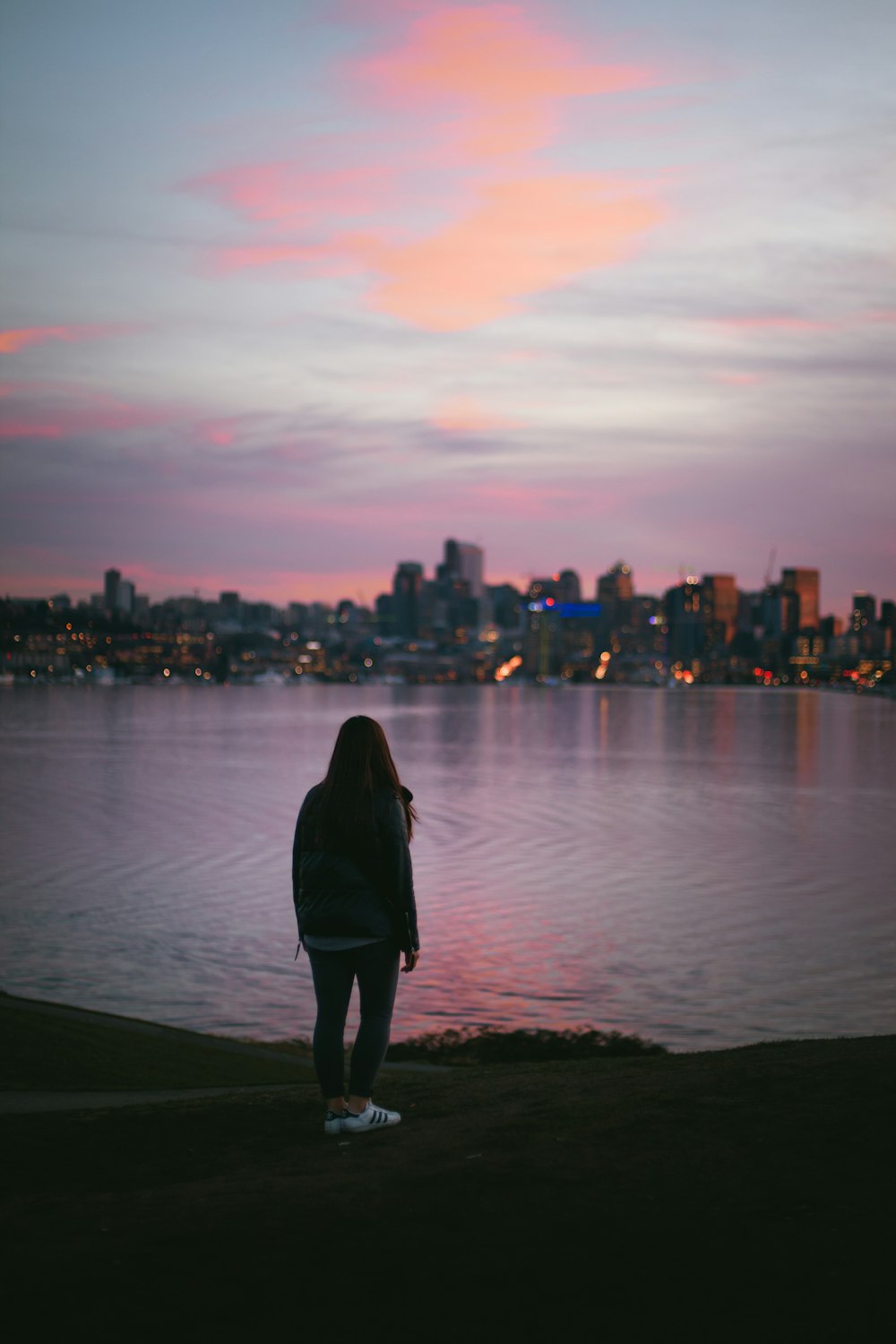 woman in black coat standing on seashore during sunset