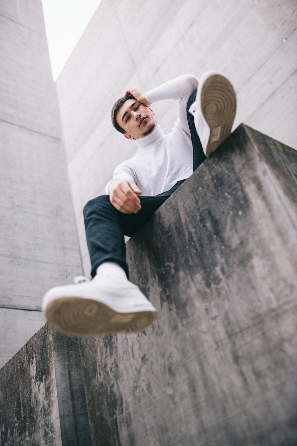 man in white long sleeve shirt and black pants sitting on concrete wall during daytime