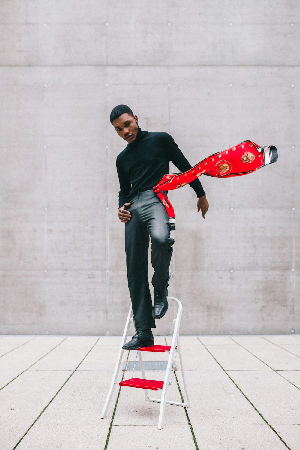 man in black sweater and gray pants standing beside red and white skateboard