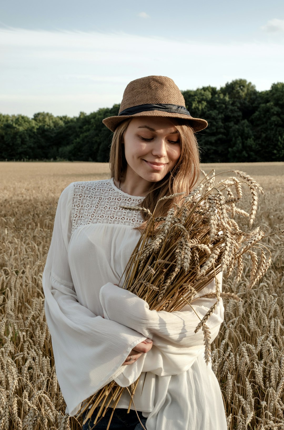 woman in white long sleeve shirt and brown hat standing on brown wheat field during daytime