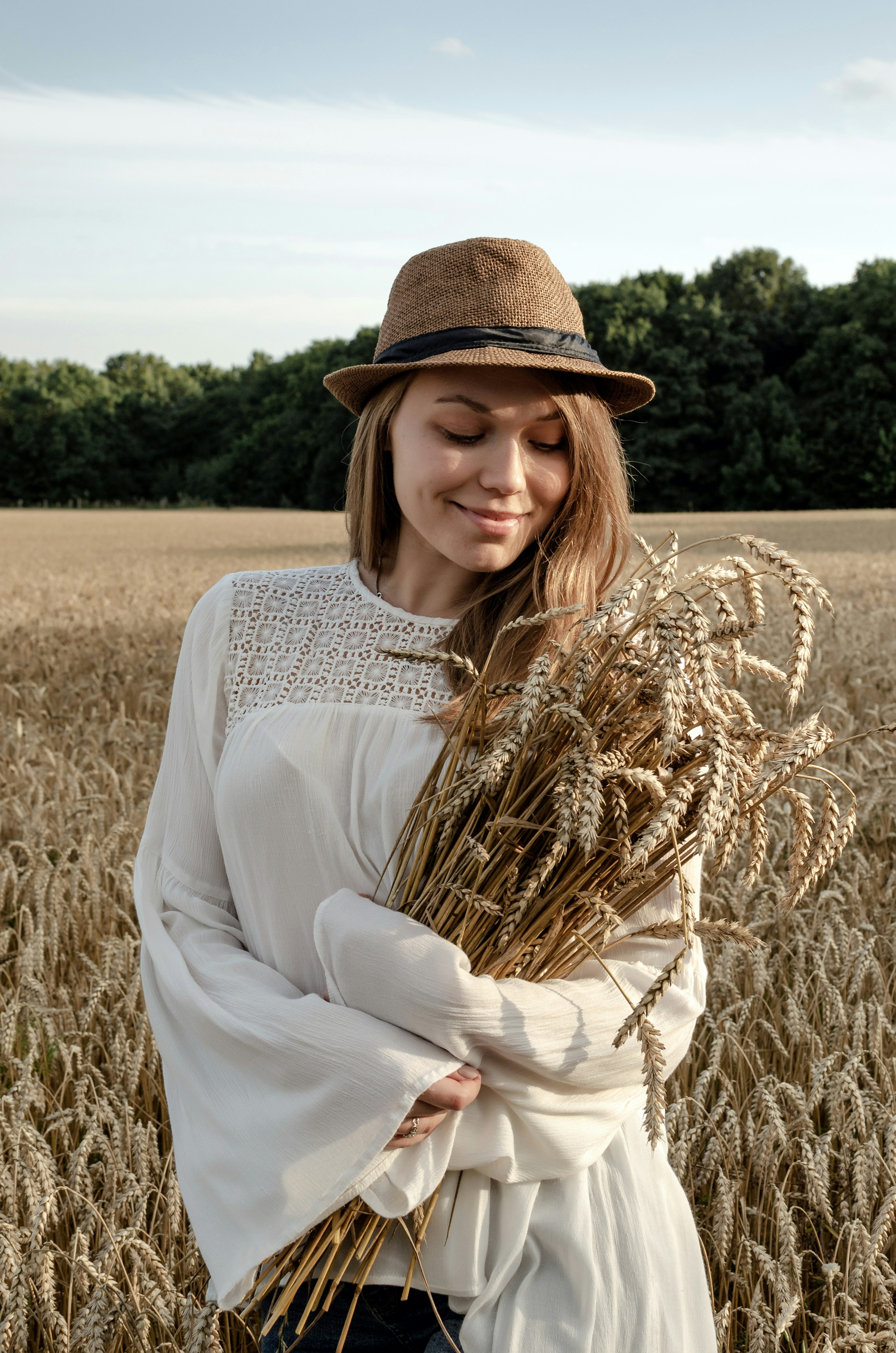 woman in white long sleeve shirt and brown hat standing on brown wheat field during daytime