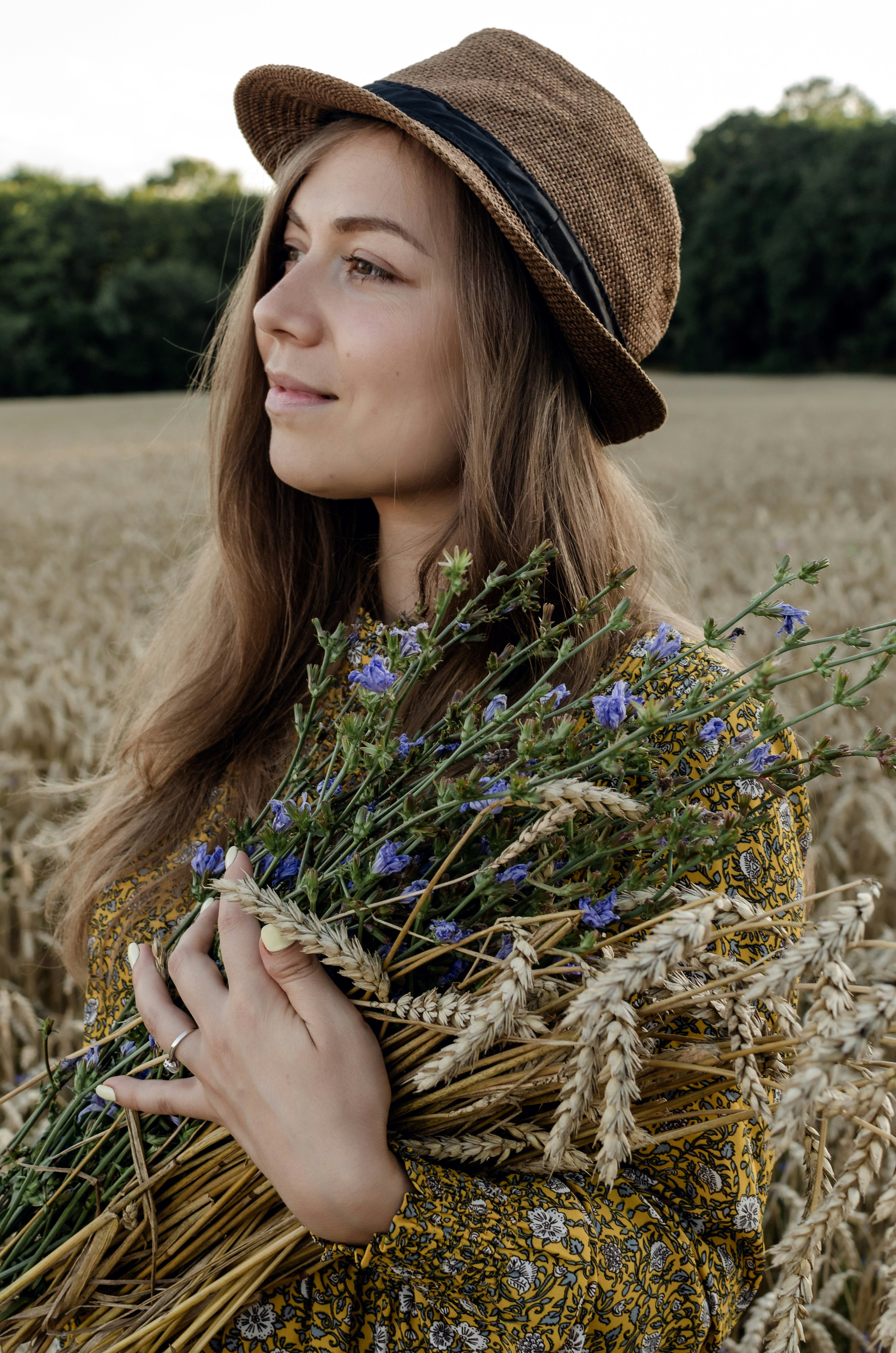 woman in blue and white floral shirt wearing brown hat holding purple flowers