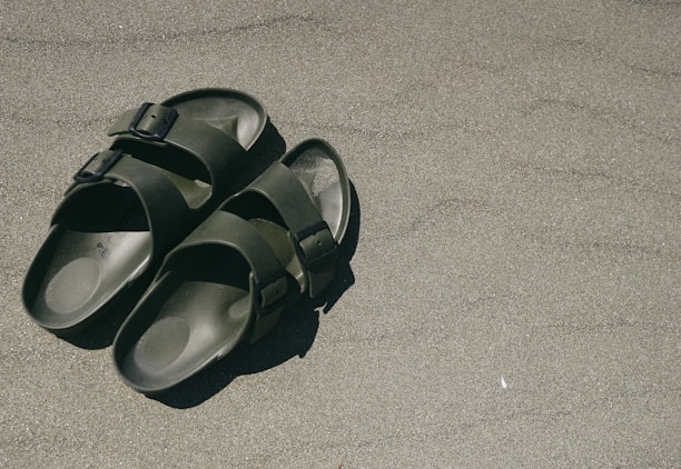 A pair of minimalist bamboo sandals placed beside green leaves, emphasizing the eco-friendly and natural materials.