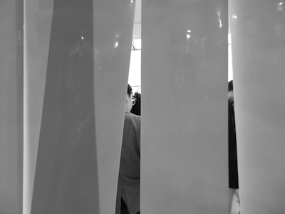 Vertical opaque panels partially obscure the view of people behind them. The space has a minimalist and modern aesthetic, with a play of light and shadows on the surfaces.
