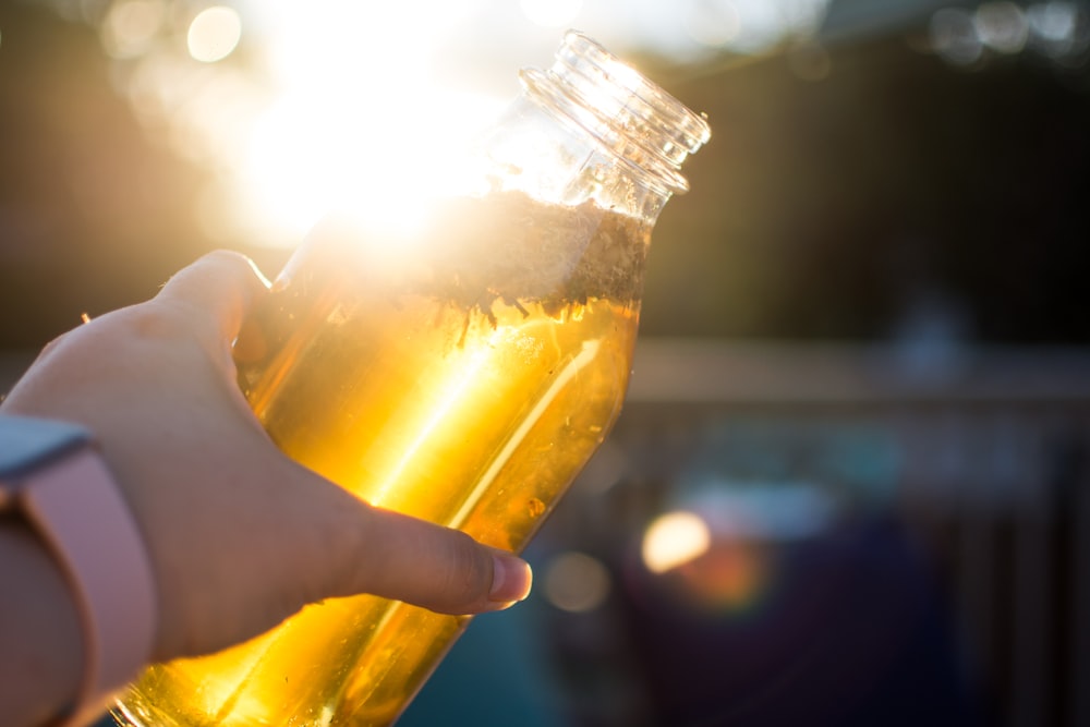 person holding clear glass jar with yellow liquid