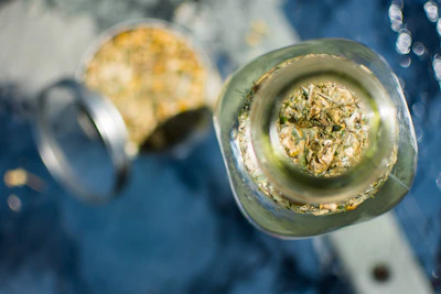 Close-up of a small jar of herbalcow ayurvedic balm surrounded by fresh green herbs and a golden cow ghee pot in the background.