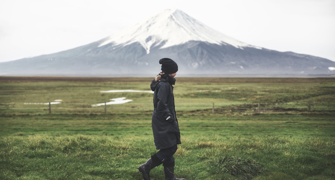 man in black jacket standing on green grass field near snow covered mountain during daytime