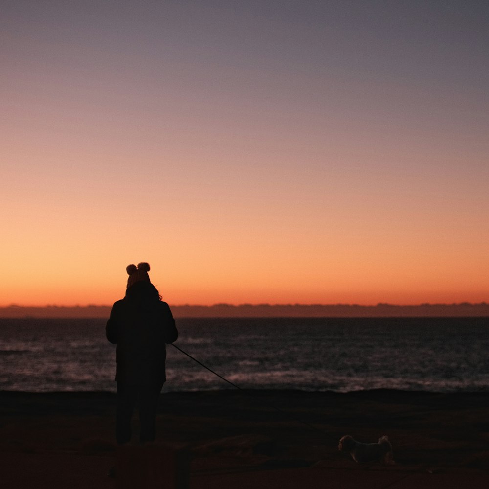 silhueta do homem de pé na costa durante o pôr do sol