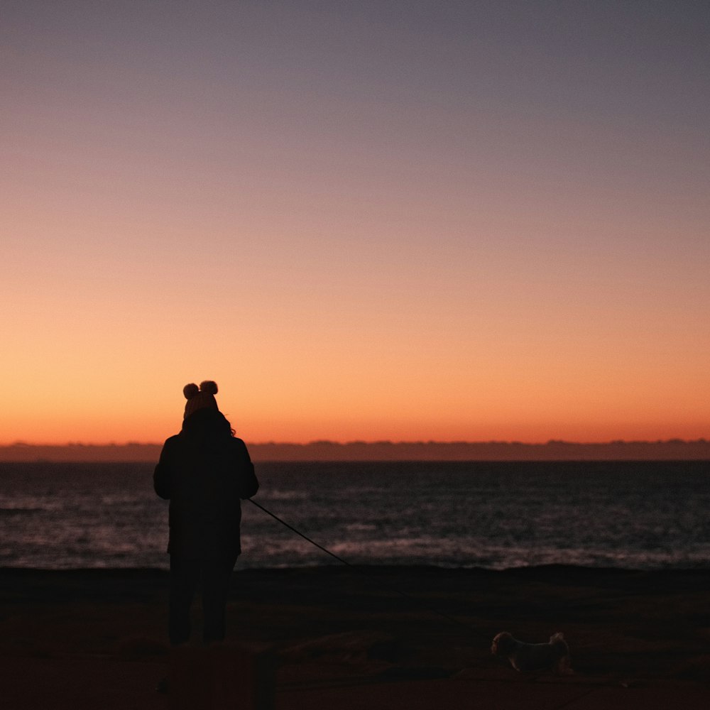 silhouette of man standing on seashore during sunset