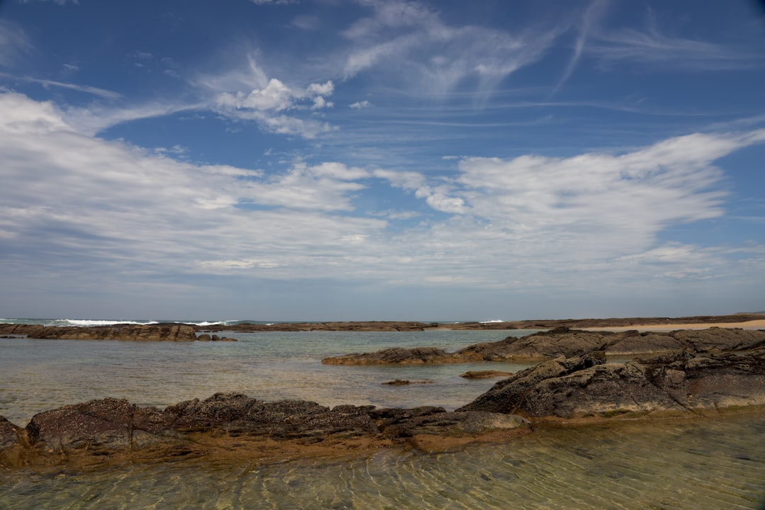 brown and black rock formation near body of water under blue and white cloudy sky during