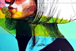 A vibrant street art mural featuring a stylized side profile of a face with bold graphic lines and vivid colors. The artwork combines brush strokes and geometric shapes with a palette of reds, greens, blues, and yellows, creating a dynamic and modern aesthetic.