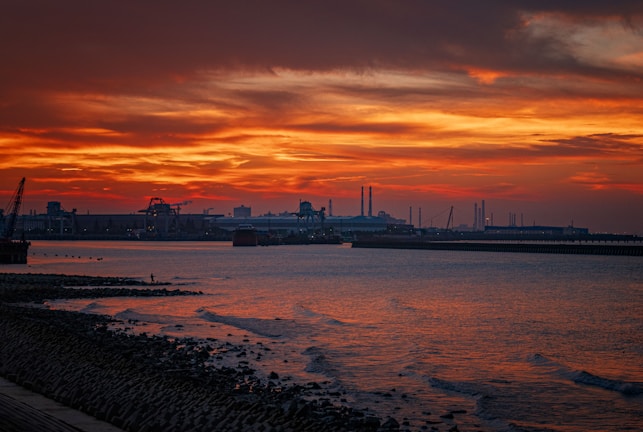 Sunrise over a coastal tank farm with calm waters reflecting the industrial landscape.