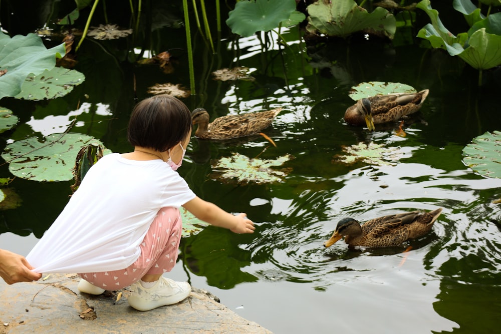 girl in pink shirt and white pants sitting on brown rock in front of lake during