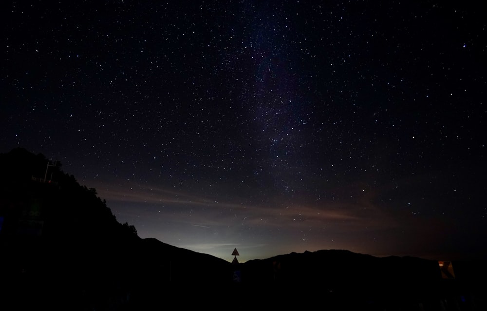 silhouette of person standing on hill under starry night