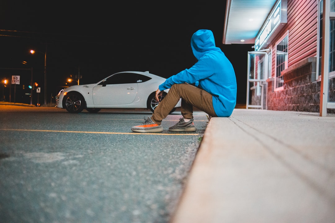 man in blue hoodie and blue pants sitting on gray concrete floor
