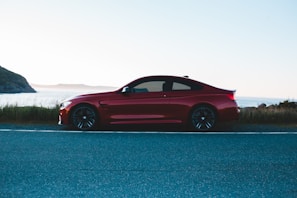 A sporty red coupe speeding along a coastal highway, the ocean sparkling in the background.