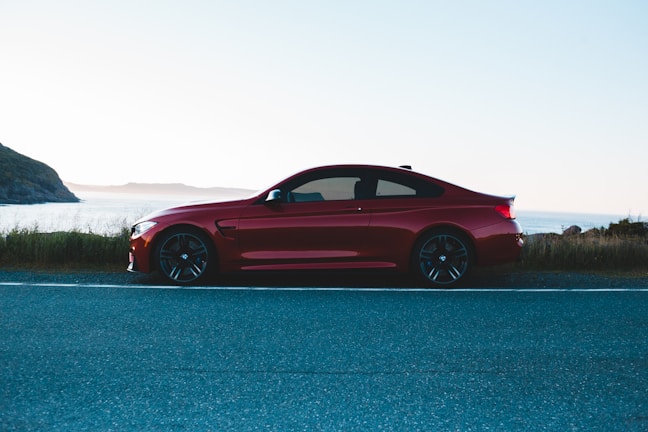 Sleek red sports car parked on a coastal road at sunset.