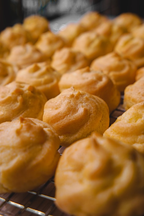 A close-up of golden, flaky cream puffs dusted with powdered sugar on a rustic wooden board.