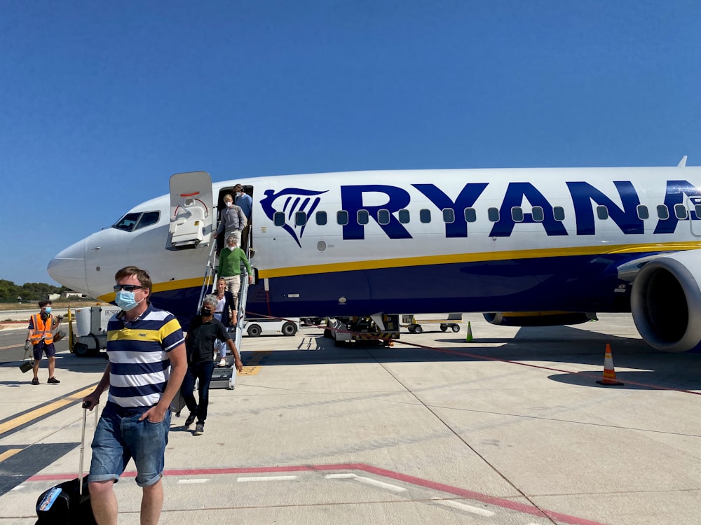 man in yellow shirt and gray shorts standing beside white and blue airplane during daytime