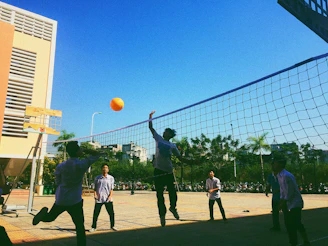 Volleyball players in blue jerseys jumping and celebrating a point outdoors under clear sky