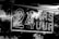 A neon sign displays the text '24 HRS 7 UUR' in bold letters. The background features reflections of trees, likely captured through a reflective surface such as glass.