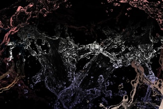 Chaotic splashes and streams of water are captured mid-movement against a dark background, creating an abstract and dynamic visual effect. The water appears in various transparent shapes and forms, giving an impression of fluidity and motion.