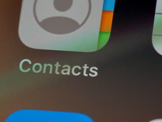 Close-up view of a smartphone screen displaying the Contacts application icon. The icon features a stylized silhouette of a person alongside multicolored gradients. Below the icon, the word 'Contacts' is clearly visible against a gray background.